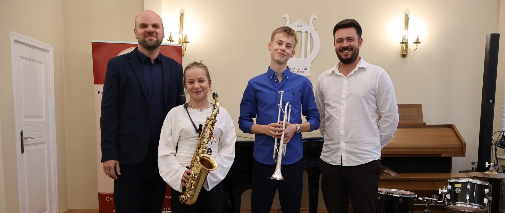 Uczniowie trzymający w dłoniach instrumenty muzyczne, Po bokach nauczyciele.
