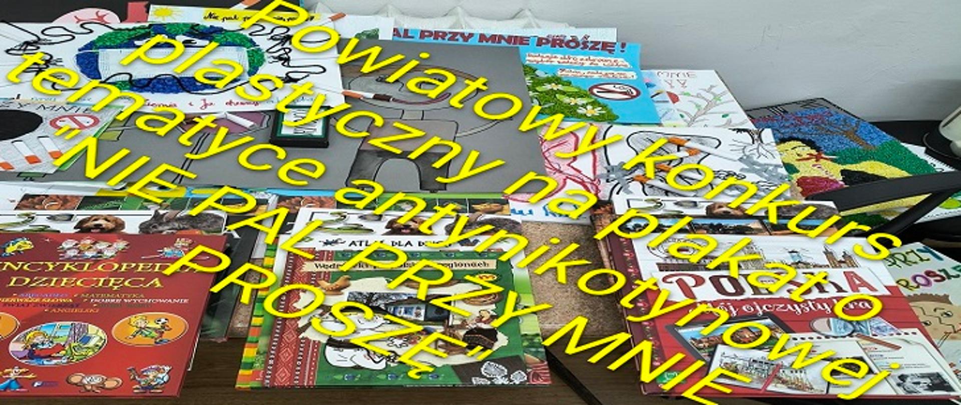 Na stole leży duża liczba kolorowych książek, zeszytów i prac plastycznych przygotowanych przez dzieci. Na zdjęciu umieszczono duży żółty napis informujący o „Powiatowym Konkursie Plastycznym na plakat tematyce antynikotynowej „NIE PAL PRZY MNIE, PROSZĘ””. Całość przedstawia ekspozycję materiałów związanych z konkursem promującym postawy prozdrowotne i profilaktykę antynikotynową wśród dzieci.