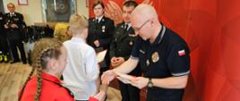 fotografia przedstawia uczestników konkursu w trakcie wręczania dyplomów, w tle ścianka Państwowa Straż Pożarna, część wyposażenia Sali