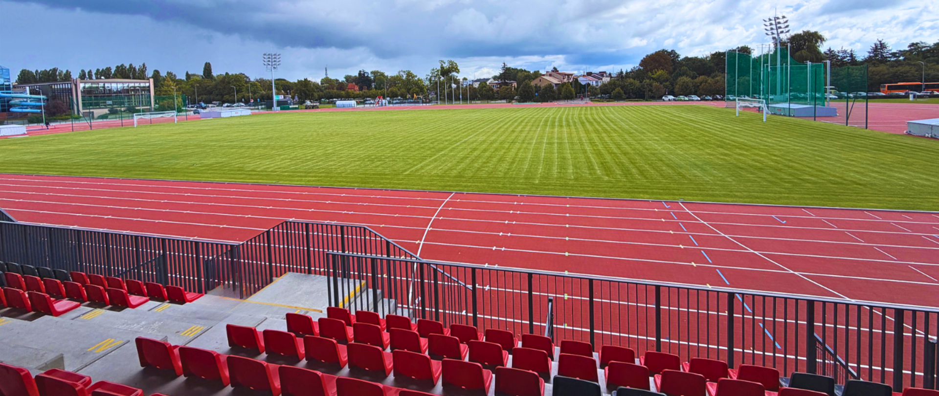 Widok na stadion w Płońsku z czerwonymi trybunami, bieżnią lekkoatletyczną i boiskiem piłkarskim.