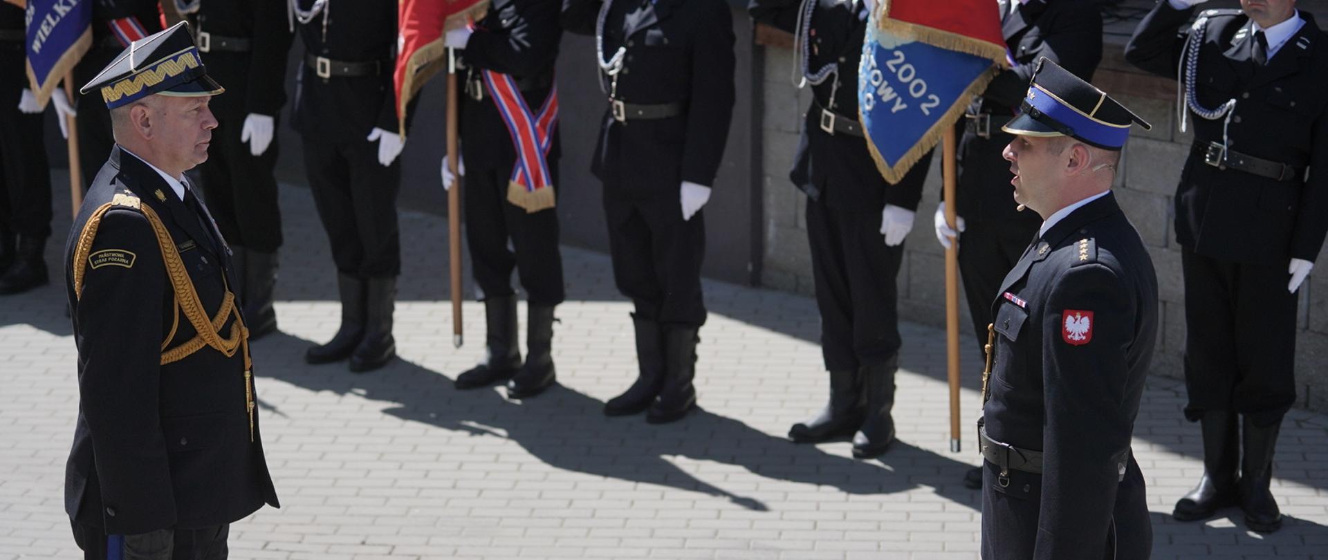 Dowódca uroczystości składa meldunek z-cy komendanta głównego PSP. W tle poczty sztandarowe