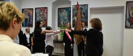 Na zdjęciu przedstawiono uroczyste ślubowanie uczniów. Młodzież w eleganckich strojach składa przysięgę, uczestnicząc w ważnej ceremonii szkolnej. Uroczystości towarzyszy podniosła atmosfera, a w tle widoczne są obrazy i dekoracje.