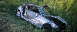 Zdjęcie przedstawia rozbity samochód osobowy w przydrożnym rowie, zdjęcie wykonane od strony przodu pojazdu.