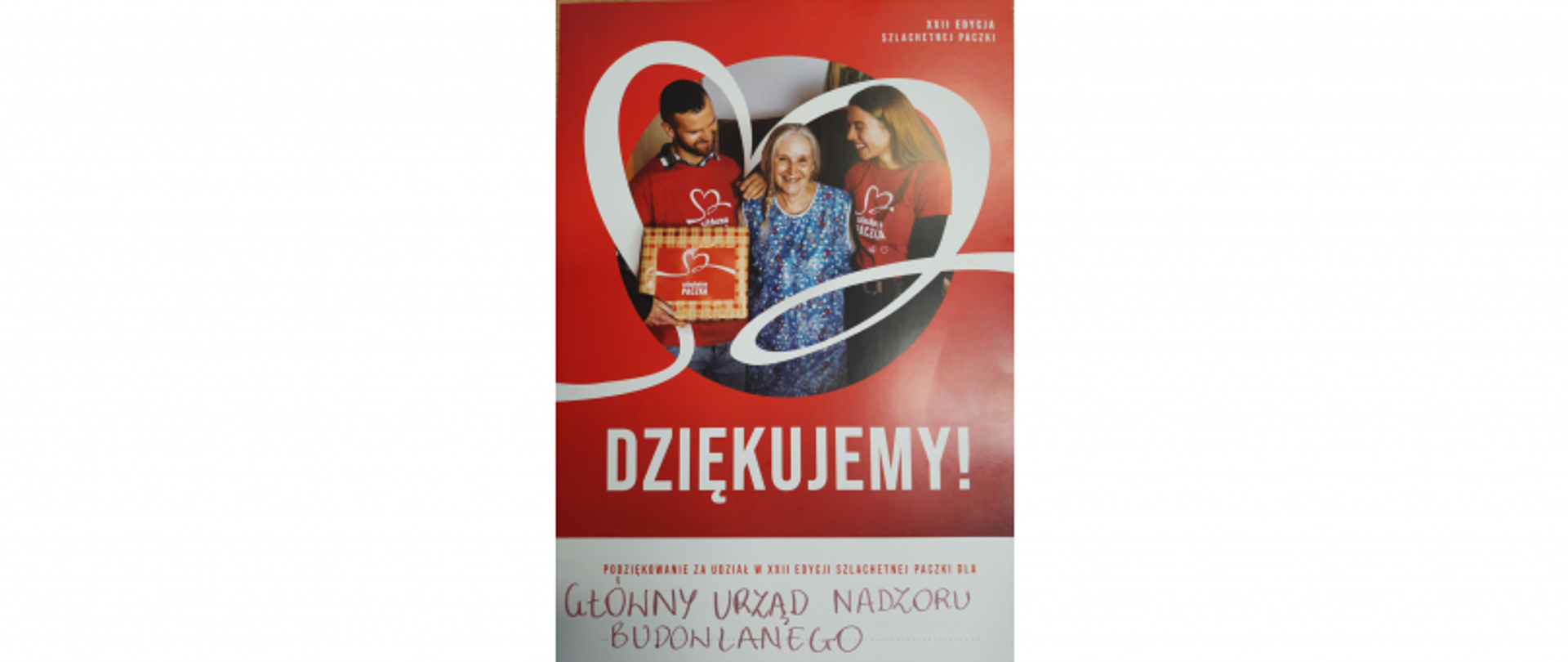 Trzy osoby z pudełkiem z sercem, plakat z napisem „Dziękujemy! Podziękowanie za udział w XVIII edycji Szlachetnej Paczki 2018”, podpis: Główny Urząd Nadzoru Budowlanego.