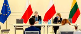 Minister siedzi za stołem, za nim flagi Polski, Litwy i UE.