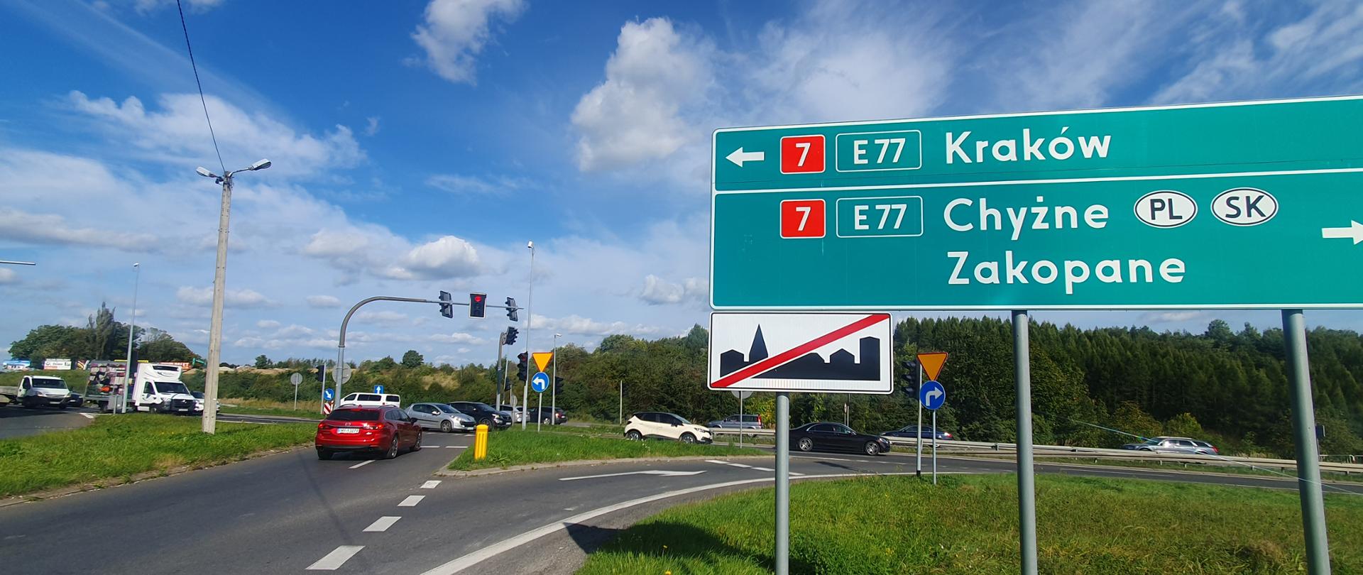 Zdjęcie lokalizacji przyszłego węzła w Myślenicach. Skrzyżowanie z widoczną tablicą wskazującą kierunki na Kraków (strzałka w lewo), na Chyżne i Zakopane (strzałka w prawo). Pod tablicą, znak: koniec terenu zabudowanego. 