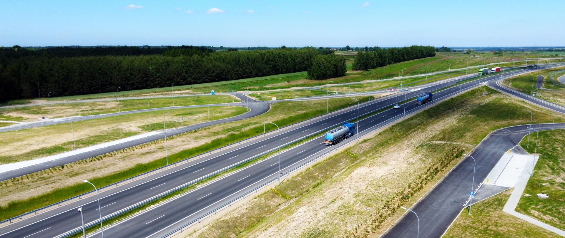 Droga ekspresowa S19 na odc. Łowisko - Sokołów Młp, świeci słońce, sceneria wiosenna, widać drogę oraz jadące po niej ciężarówki