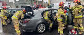Dwa samochody w środku strażacy udzielają pomocy poszkodowanemu