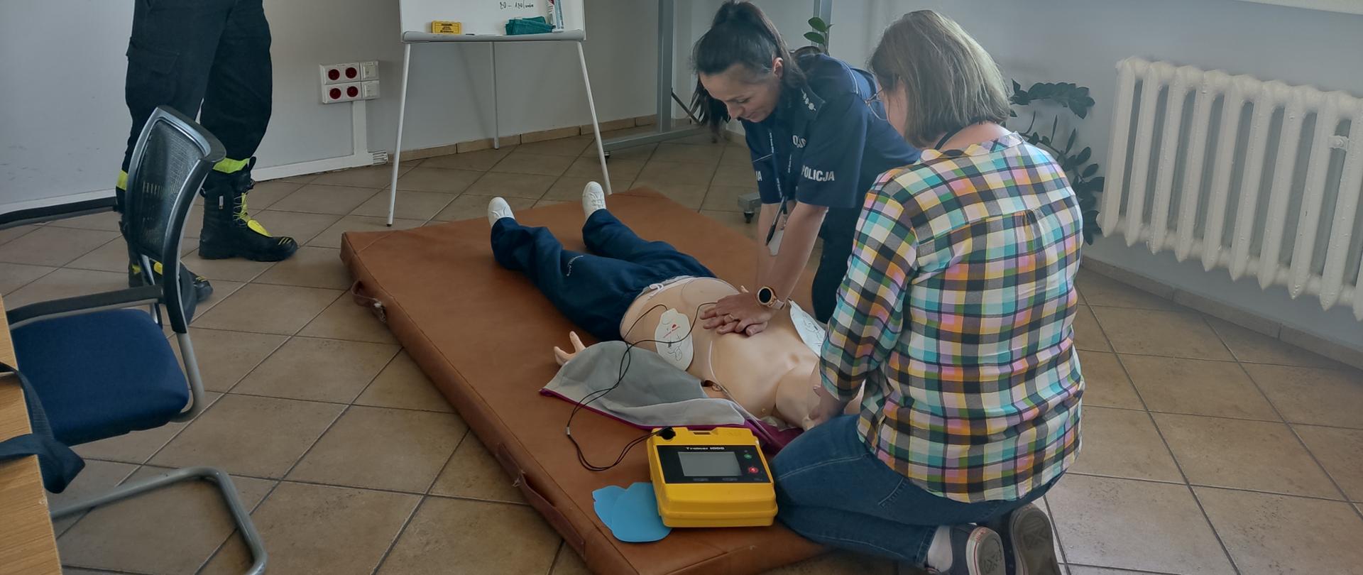 Strażak instruuje policjantów z zakresu pierwszej pomocy przy użyciu defibrylatora oraz fantomu.