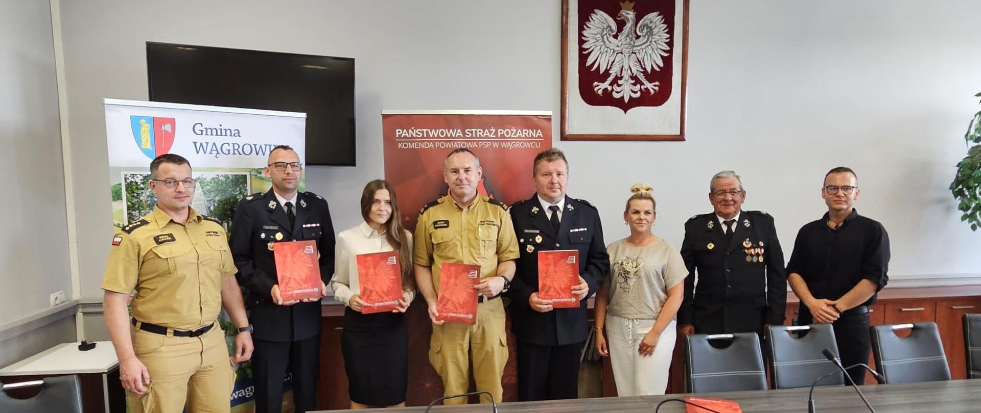 Na zdjęciu widać strażaków oraz urzędników po podpisaniu porozumienia na tle godła 