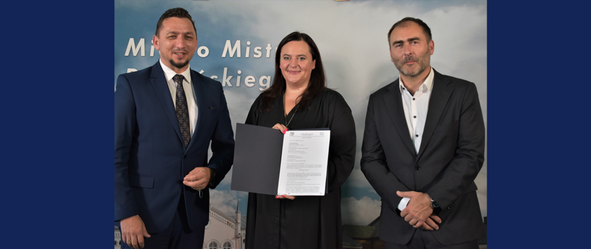 Trzy osoby stoją obok siebie. Pośrodku wiceminister Małgorzata Jarosińska-Jedynak przezentuje dokument.