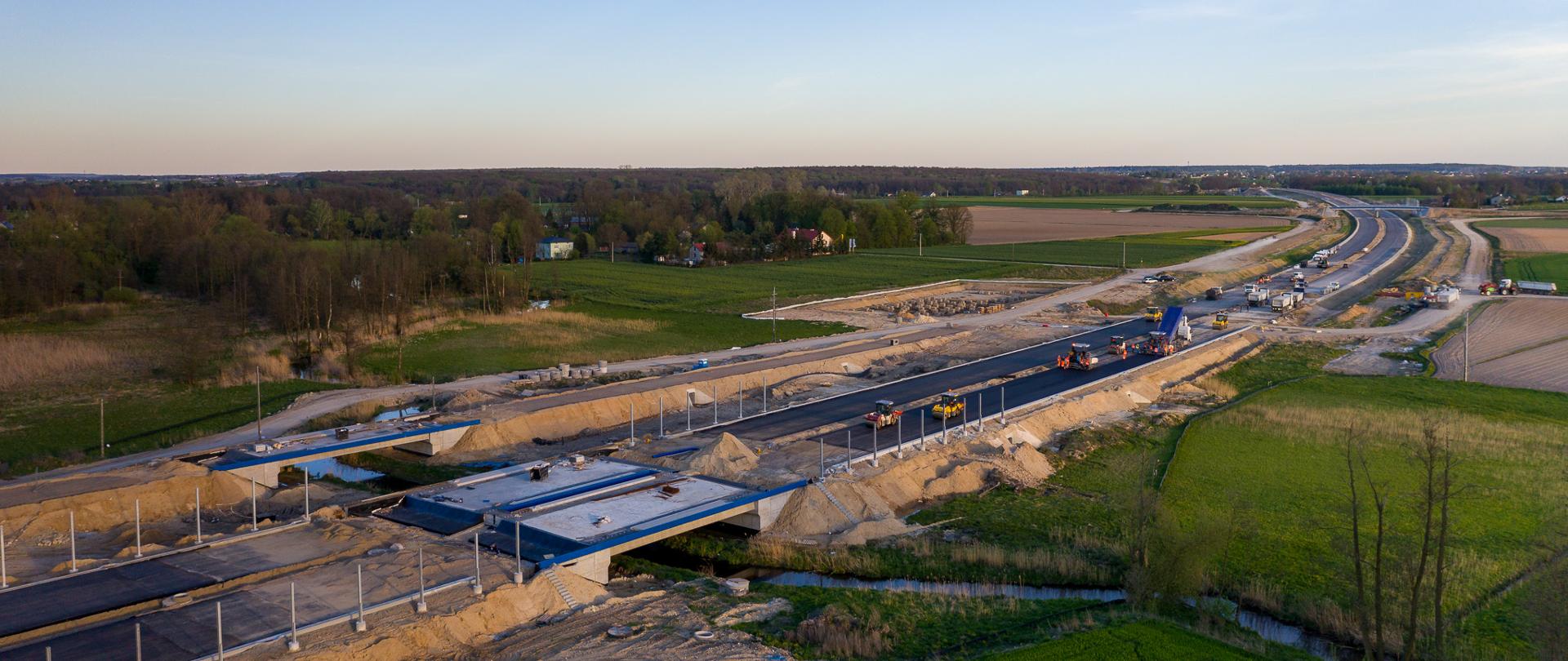 Na zdjęciu widoczne są prace na S19 Lublin - Niedrzwica. W tle widoczny las i zabudowania mieszkalne.