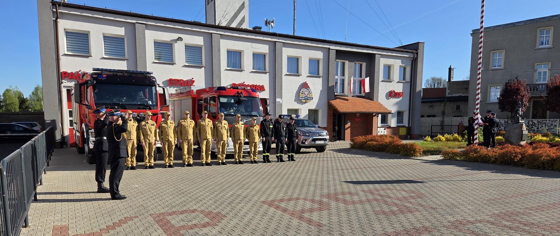 W czwartek 2 maja 2024 roku o godzinie 8:00 na placu zewnętrznym Komendy Powiatowej Państwowej Straży Pożarnej w Krotoszynie odbyła się uroczysta zmiana służby, podczas której uczczono Święto Flagi Państwowej. Strażacy stoją w szeregu na placu, trwa odśpiewanie hymnu i podniesienie flagi na maszcie. 