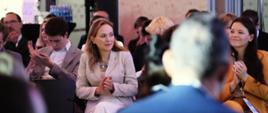 Minister Katarzyna Pełczyńska-Nałęcz siedzi na krześle i klaszcze, obok niej siedzą uczestnicy spotkania 