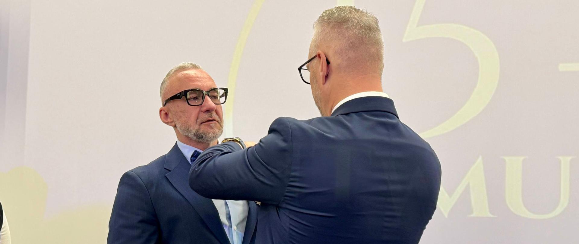 Mężczyzna w garniturze, wojewoda, przypina odznaczenie 
