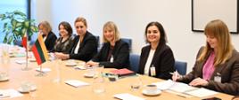 Przy stole konferencyjnym siedzi sześć kobiet, z których dwie czytają dokumenty, a cztery uśmiechają się do kamery