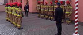 Zdjęcie przedstawia strażaków ubranych w mundury koloru musztardowego ustawionych. naprzeciwko siebie. Pomiędzy stoją strażacy ubrani w mundury wyjściowe koloru czarnego. Trwa ślubowanie