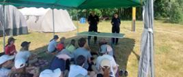 W tele widać policjantkę i strażaka, którzy przekazują informację młodzieży jak zachowywać się na obozie harcerskim.