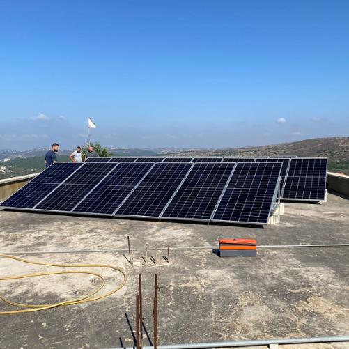 Panele fotowoltaiczne na dachu budynku, w tle widać wzgórza