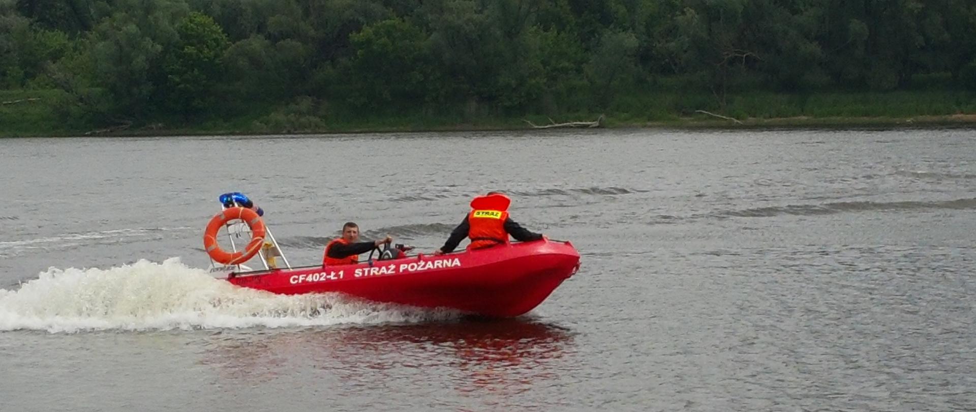 Zdjęcie przedstawia czerwoną łódź strażacką i obsługującego nią strażaka na rzece Wisła