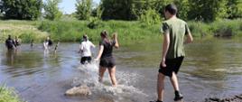zawodnicy wbiegają do rzeki, w korycie rzeki stoi dwóch strażaków ubranych w skafandry, zabezpieczają zawodników wchodzących do wody