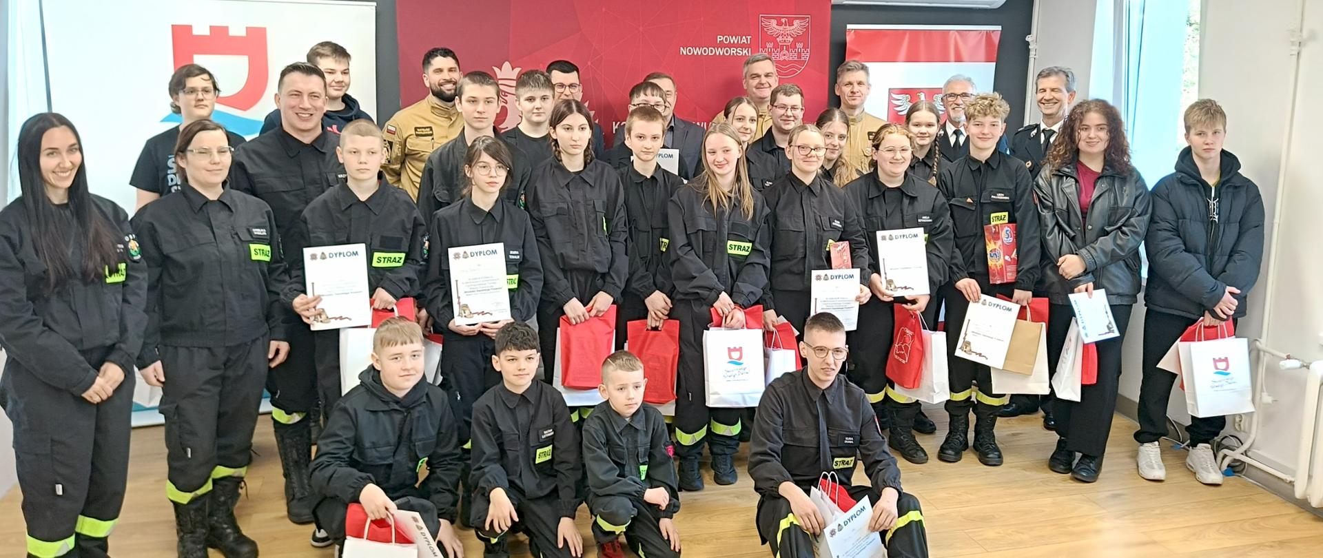 Uczestnicy turnieju, strażacy i przedstawiciele władz pozują do wspólnego zdjęcia z dyplomami i nagrodami. Na zdjęciu oprócz dzieci i młodzieży uczestniczącej w turniej widać także funkcjonariuszy z KP PSP NDM n czele z Komendantem Powiatowym st. bryg. Stanisławem Brzozowskim, jest również Wice Starosta nowodworski oraz Wice Burmistrz Miasta Nowy Dwór Mazowiecki. Na zdjęciu są również przedstawiciele ZOSP RP na czele Prezesa Zarządu Powiatowego Druha Andrzeja Hiszpańskiego.