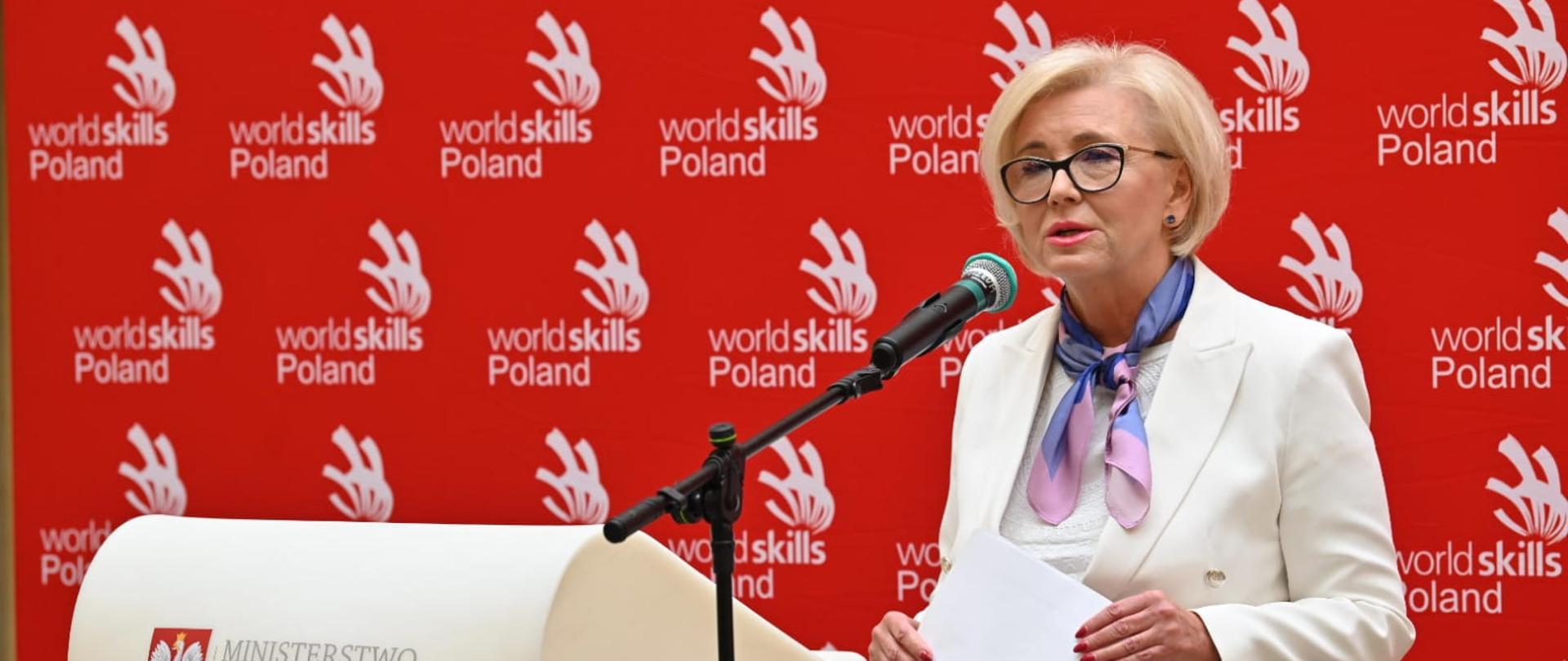 Minister Machałek stoi i mówi do mikrofonu, za nią czerwona ścianka, przed nią mównica z napisem FRSE.