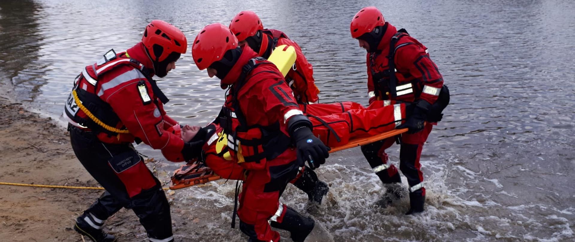 czterech ratowników wynoszących z wody poszkodowanego na noszach typu deska 