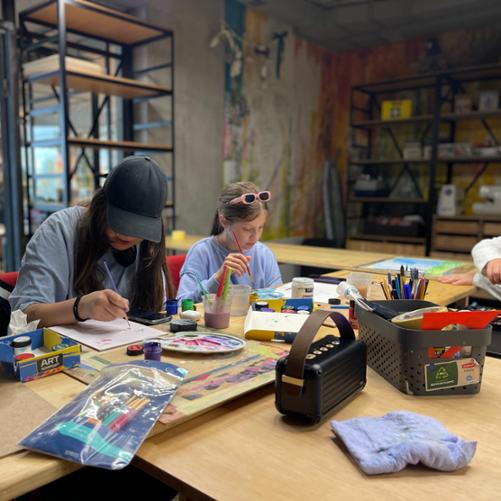 Przy stole siedzą uczestnicy zajęć i malują obrazki przy użyciu farb