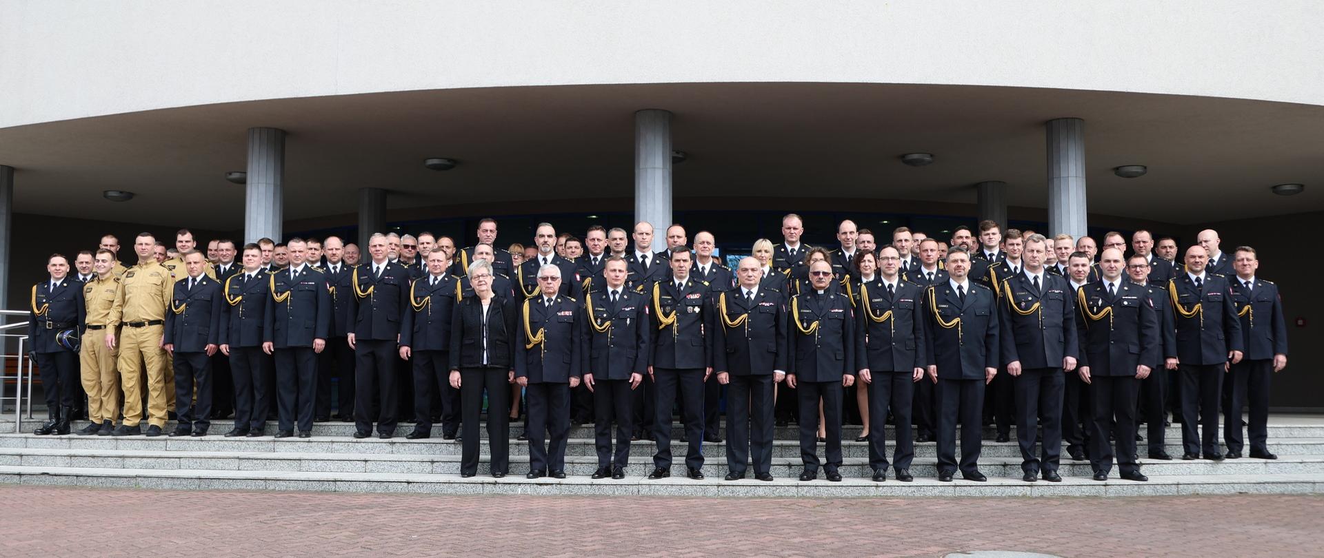 Pamiątkowa fotografia uczestników powołania komendanta Centralnej Szkoły Państwowej Straży Pożarnej w Częstochowie. Uczestnicy stoją na schodach przed budynkiem szkoły.