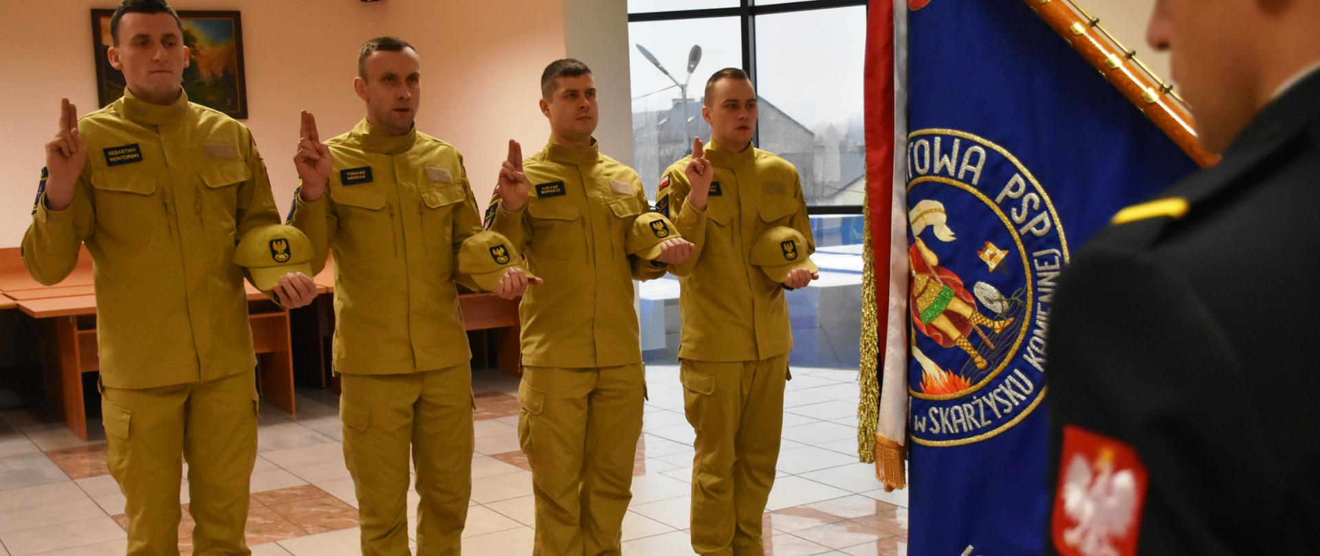 Nowo przyjęci strażacy stoją przed sztandarem wymawiając rotę ślubowania strażaka Państwowej Straży Pożarnej. W tle widać innych funkcjonariuszy KP PSP w Skarżysku-Kamiennej.