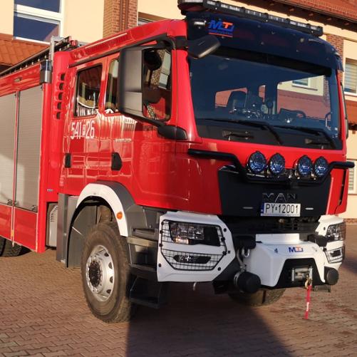 Na zdjęciu ciężki samochód gaśniczy marki MAN na placu manewrowym przed garażami Jednostki Ratowniczo-Gaśniczej