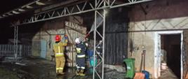 Na zdjęciu strażacy gaszą wodą palące się wrota do stodoły. Zdjęcie wykonane porą nocną.