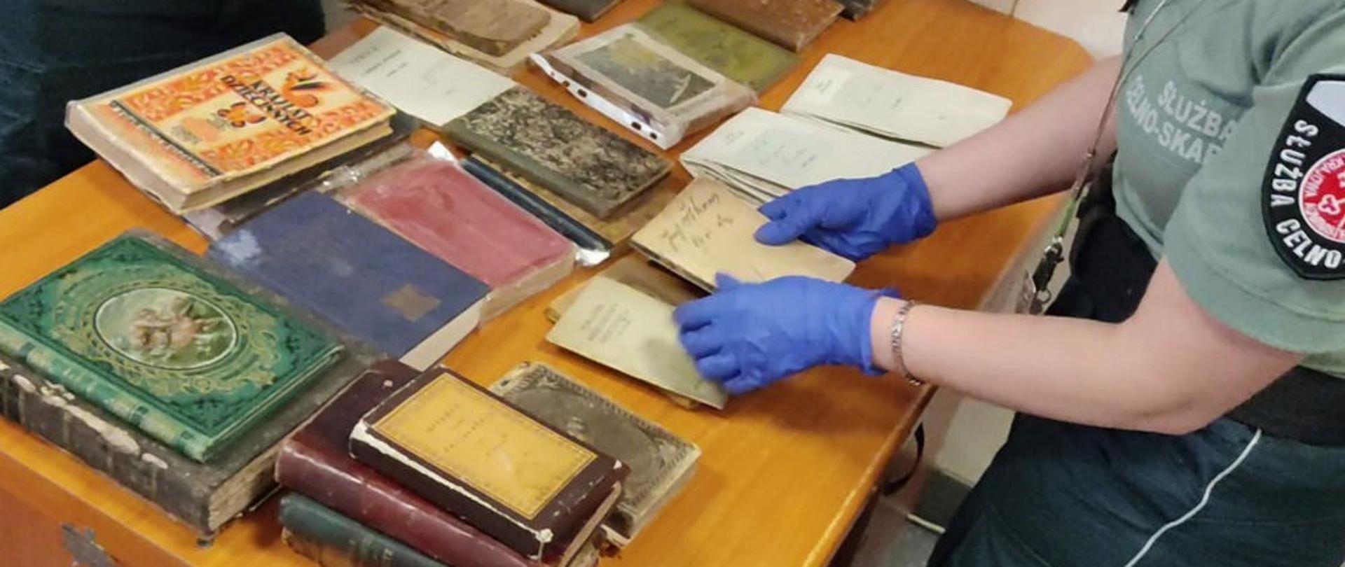 Funkcjonariuszka Służby Celno-Skarbowej rozkłada na stole zabytkowe książki.