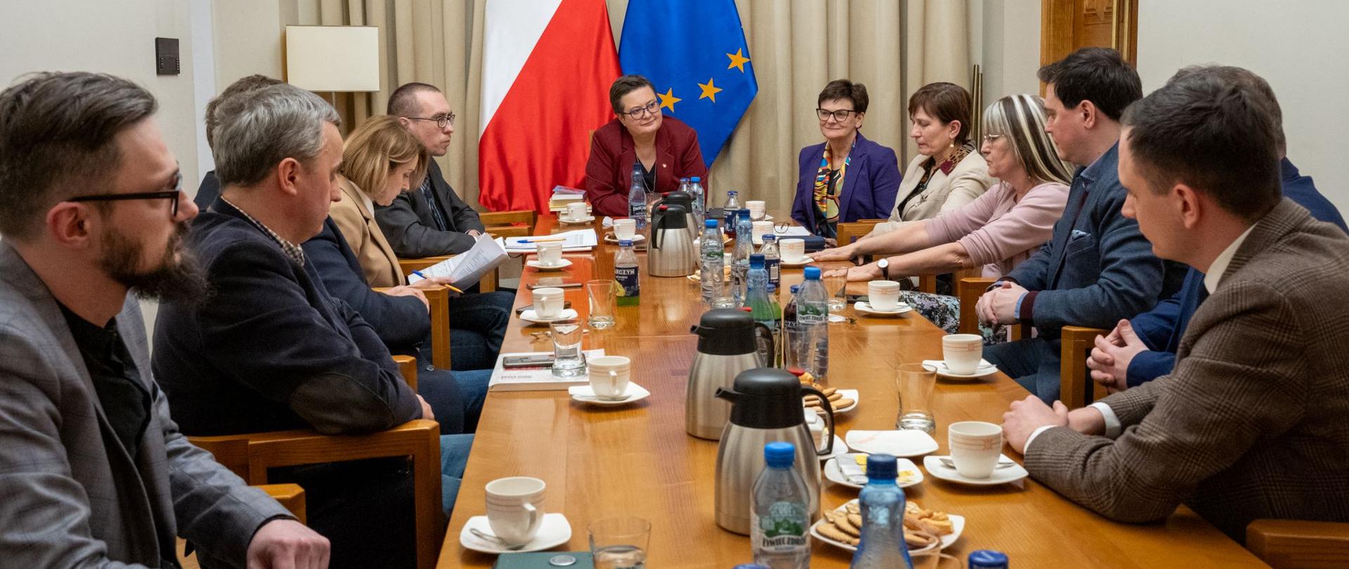 Grupa osób siedzi przy stole. na stole filiżanki, szklanki i butelki z wodą. 