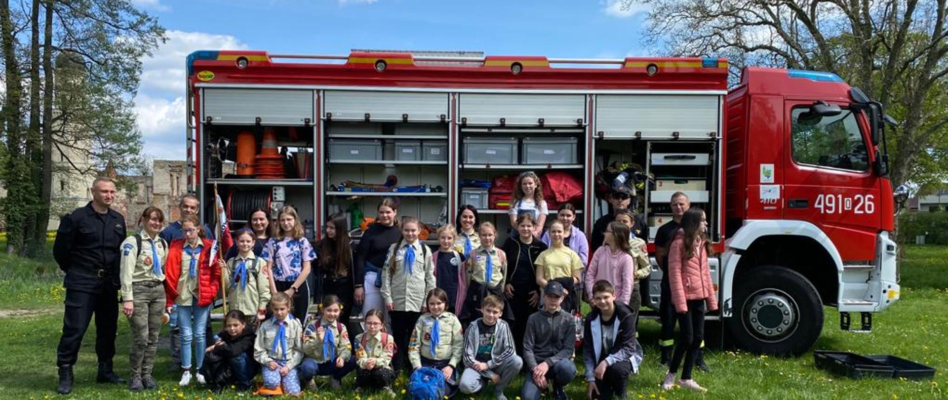 Zdjęcie przedstawia skautów i strażaków na wspólnym zdjęciu na tle samochodu strażackiego