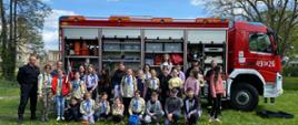 Zdjęcie przedstawia skautów i strażaków na wspólnym zdjęciu na tle samochodu strażackiego