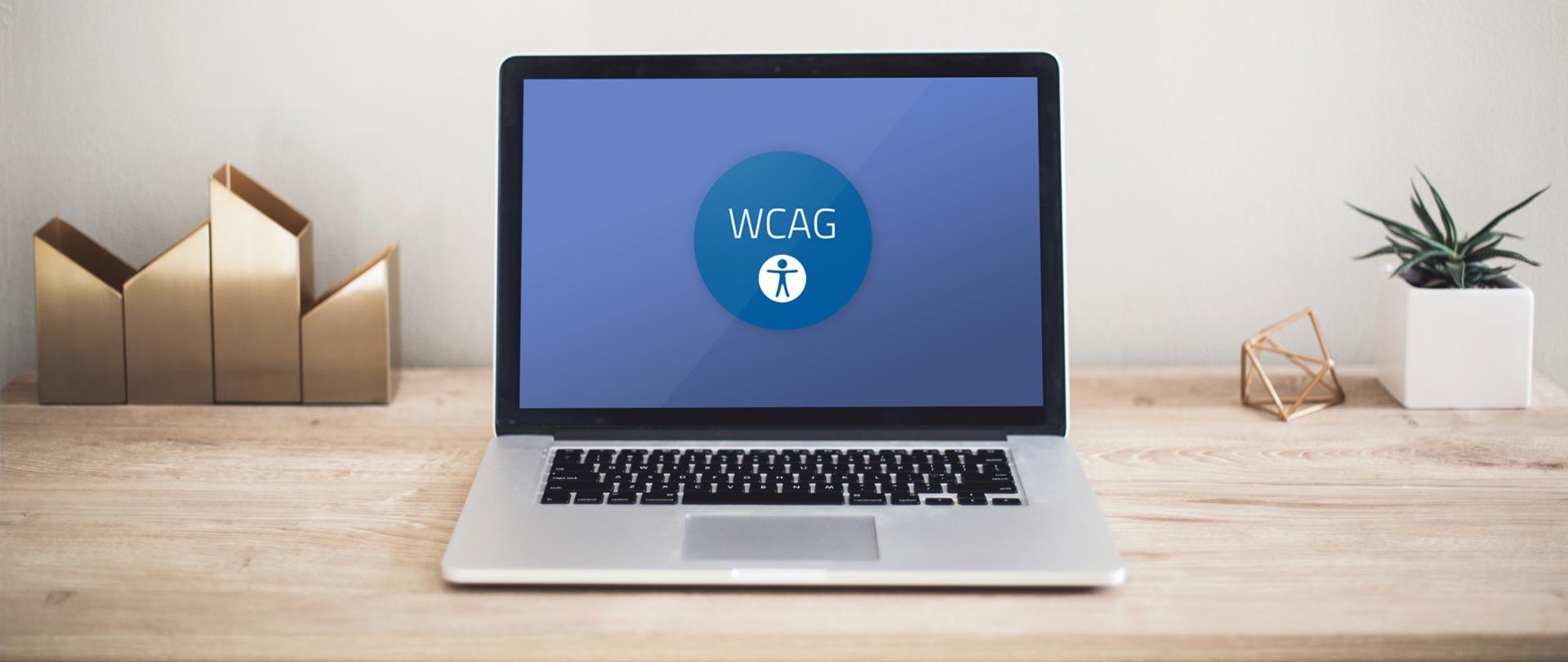 Na pierwszym planie stojący laptop na ekranie którego widoczne są litery WCAG.