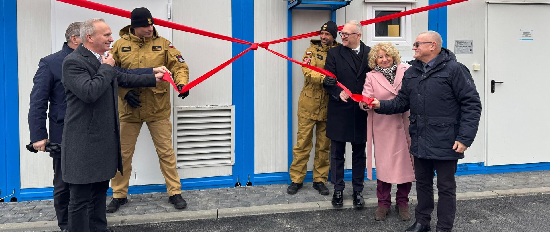Kilkanaście osób przecina wstęgę na budynku