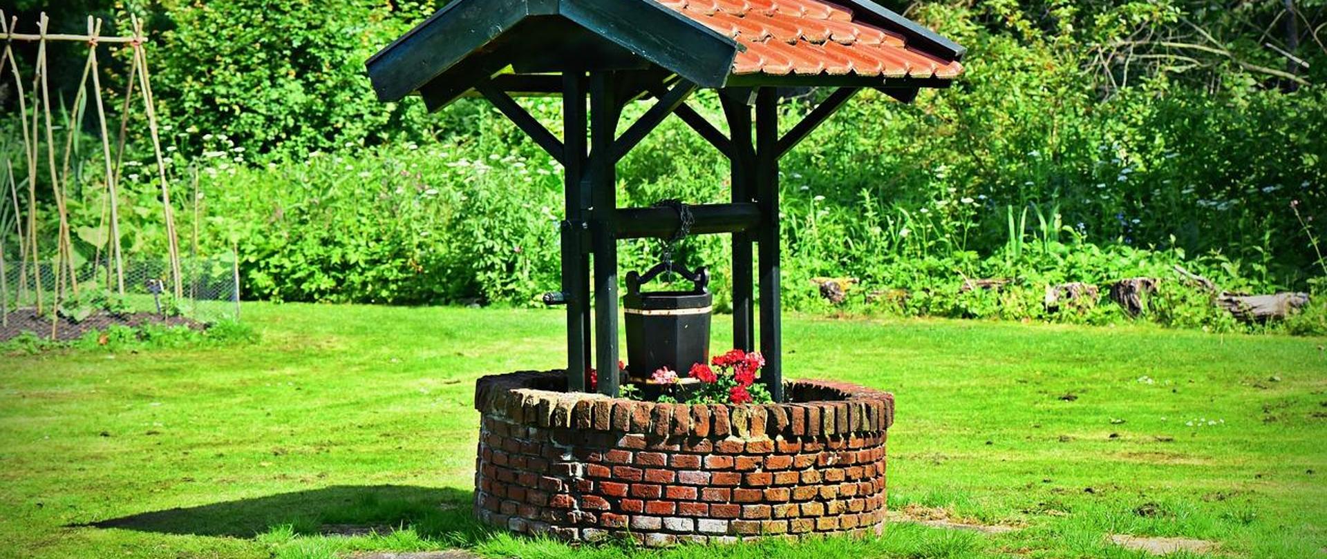 Zdjęcie studni wykonanej z cegły z dachem pokrytym dachówką. 
