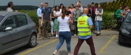 Ćwiczenia w przedsiębiorstwie hodowlano-nasiennym. Parking przed firmą, gdzie wytyczne zostało miejsce zbiórki do ewakuacji. Koordynator ewakuacji sprawdza obecność pracowników. W tle las.