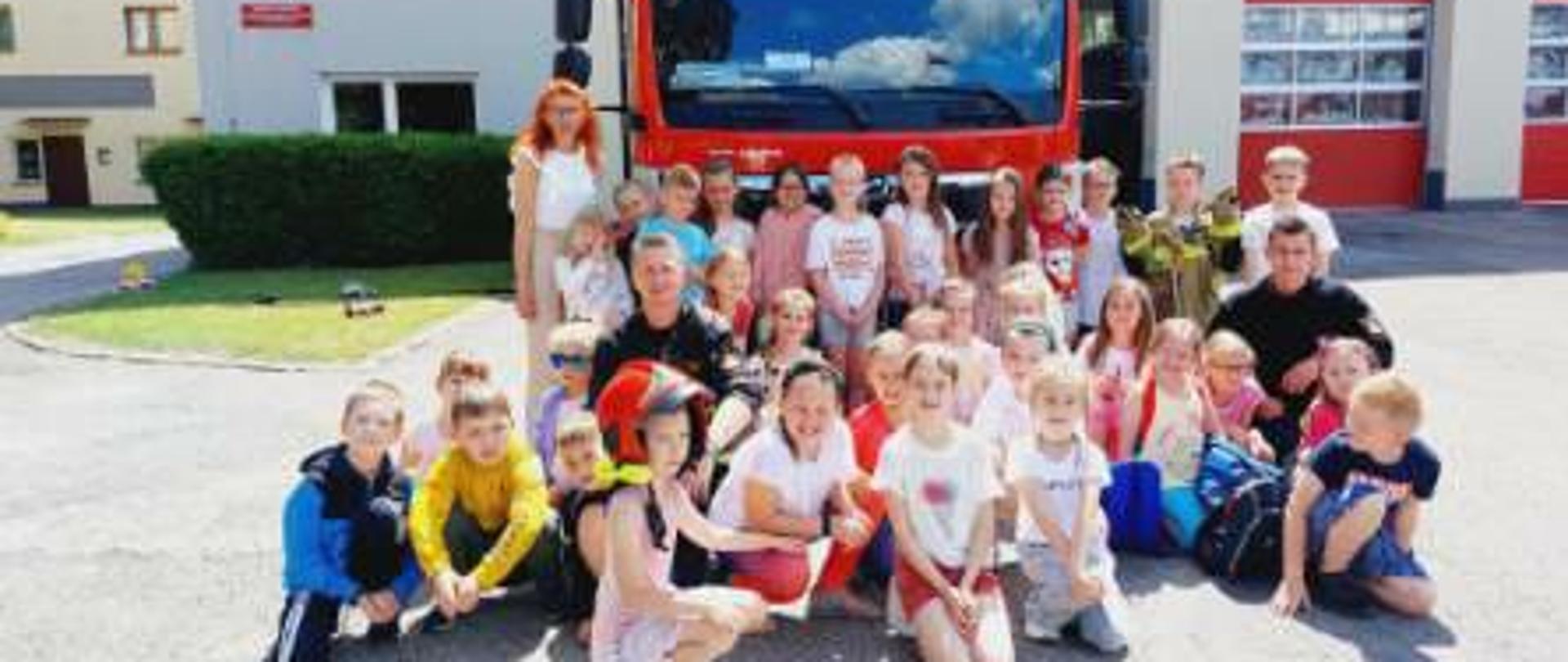 zdjęcie grupowe uczniów opiekunów i strażaków na tle samochodu, wszyscy zgromadzeniu na placu Komendy