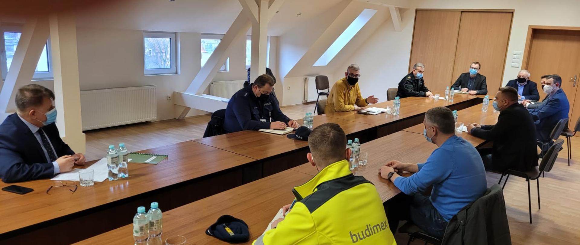 Przedstawiciele samorządów, służb i instytucji przy długim stole w sali konferencyjnej.