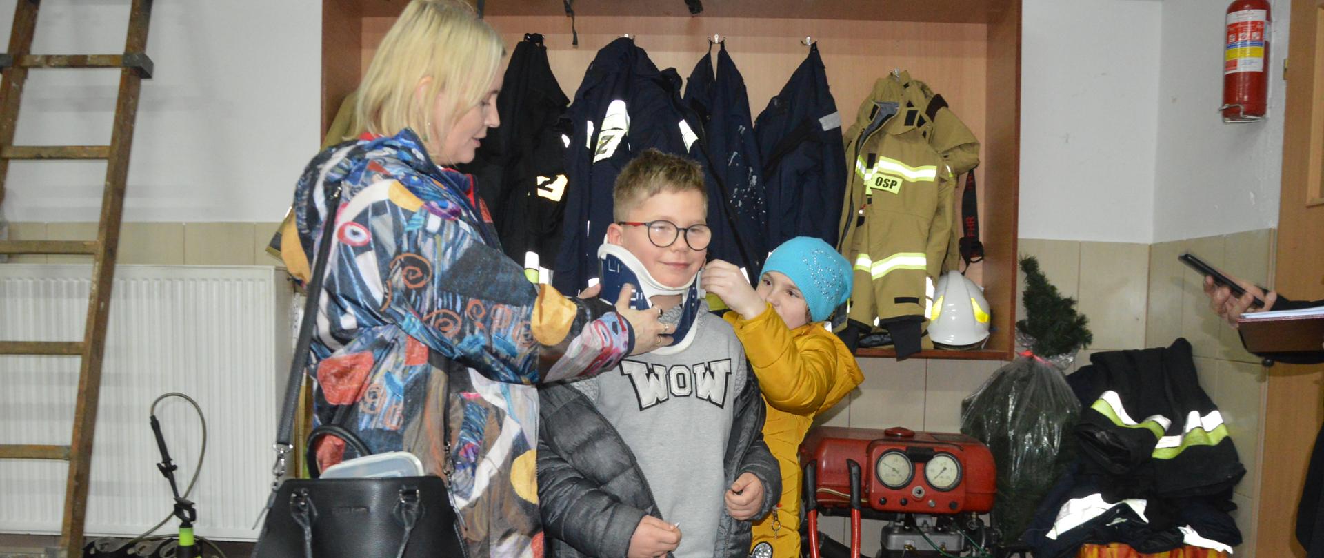 OTWP w Sobiałkowie. Garaż Ochotniczej Straży Pożarnej w Sobiałkowie. Na podłodze znajduje się sprzęt ratowniczo-gaśniczy. Uczestnicy eliminacji przygotowują się do odpowiedzi dot. nazwy wylosowanego sprzętu, jego przeznaczenia oraz zasad użycia. Jedna z uczennic wylosowała kołnierz ortopedyczny. Prezentuje w jaki sposób założyć go osobie poszkodowanej. W rolę poszkodowanego wcielił się kolega dziewczyny. W tle regał z mundurami.
