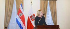 Embajadora de Polonia en México, Agnieszka Frydrychowicz-Tekieli en el podio. En el fondo las bandera de Polonia y Costa Rica.