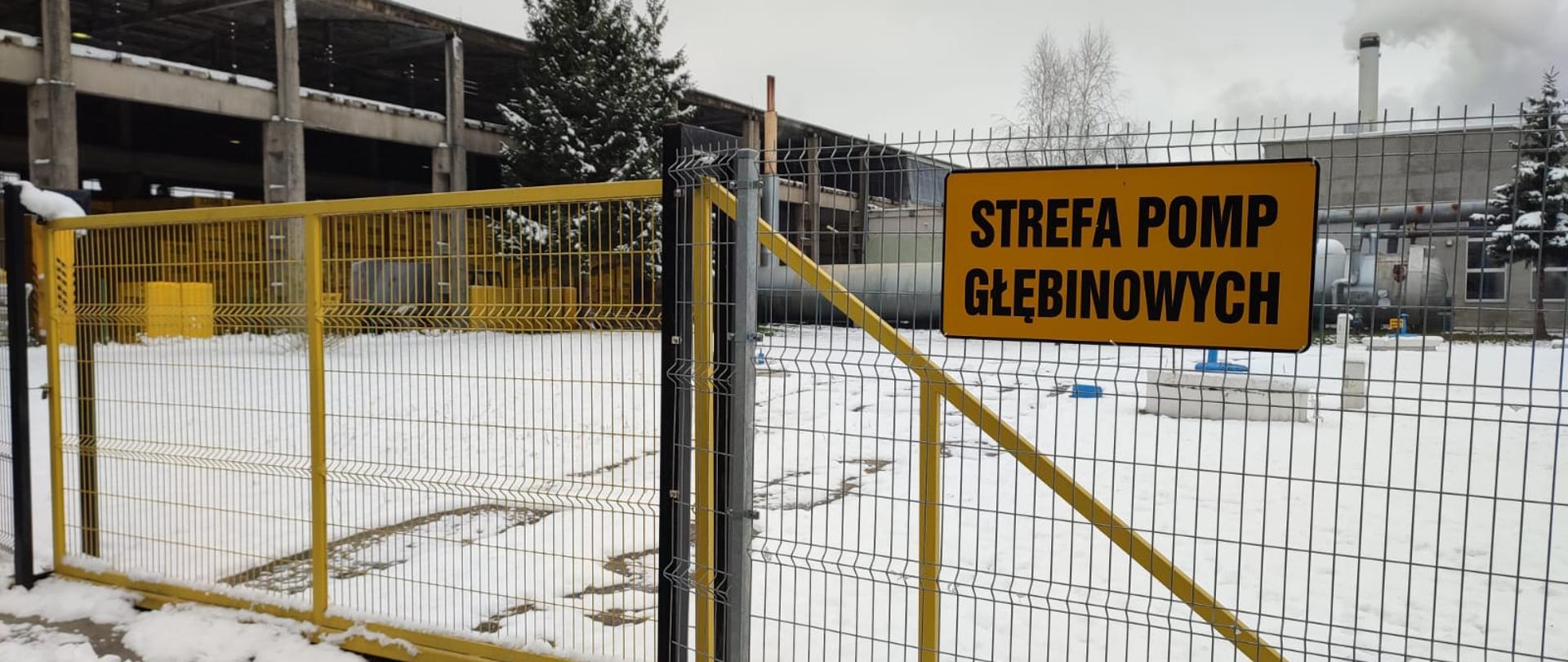 Brama wjazdowa, w oddali zakład produkcyjny.