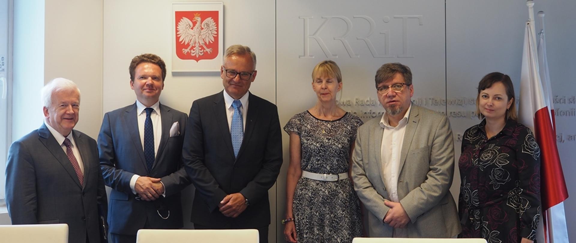 Członkowie kapituły wraz z laureatami stojący na tle białej ściany z napisem KRRiT 