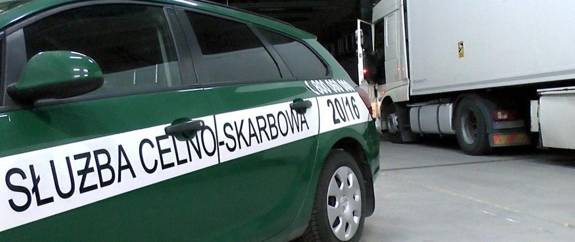 Bok radiowozu z napisem Służba Celno-Skarbowa, za nim samochód ciężarowy.