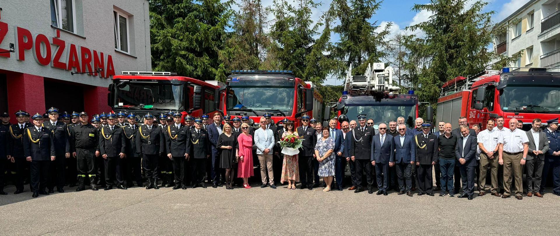 Strażacy oraz zaproszeni goście stoją na placu Komendy przed samochodami strażackimi