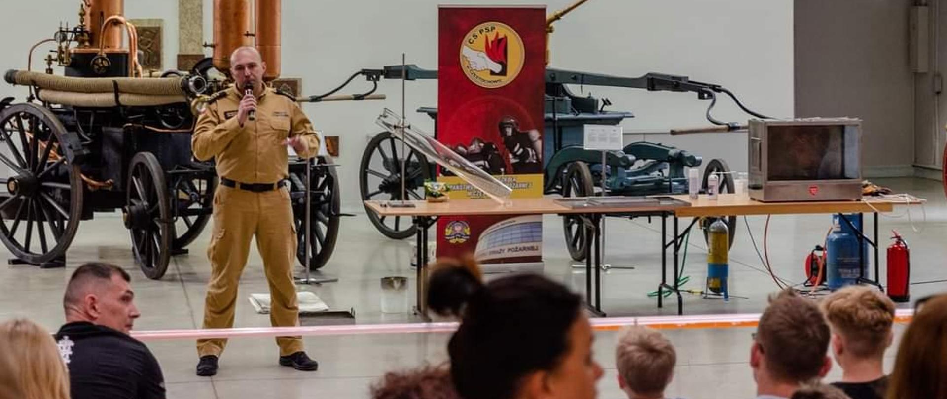 Strażak stojący na scenie i przemawiający do zgromadzonych, stojących przed nim widzów